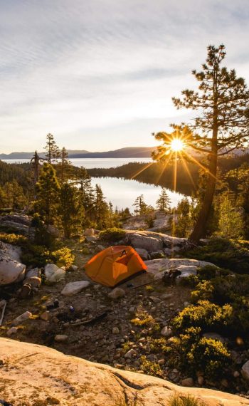 beautiful-shot-of-an-orange-tent-on-rocky-mountain-surrounded-by-trees-during-sunset-2-scaled
